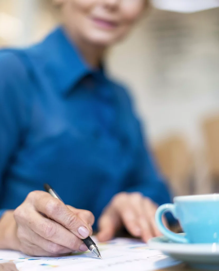 Mulher assinando documentos com uma xícara de café ao lado
